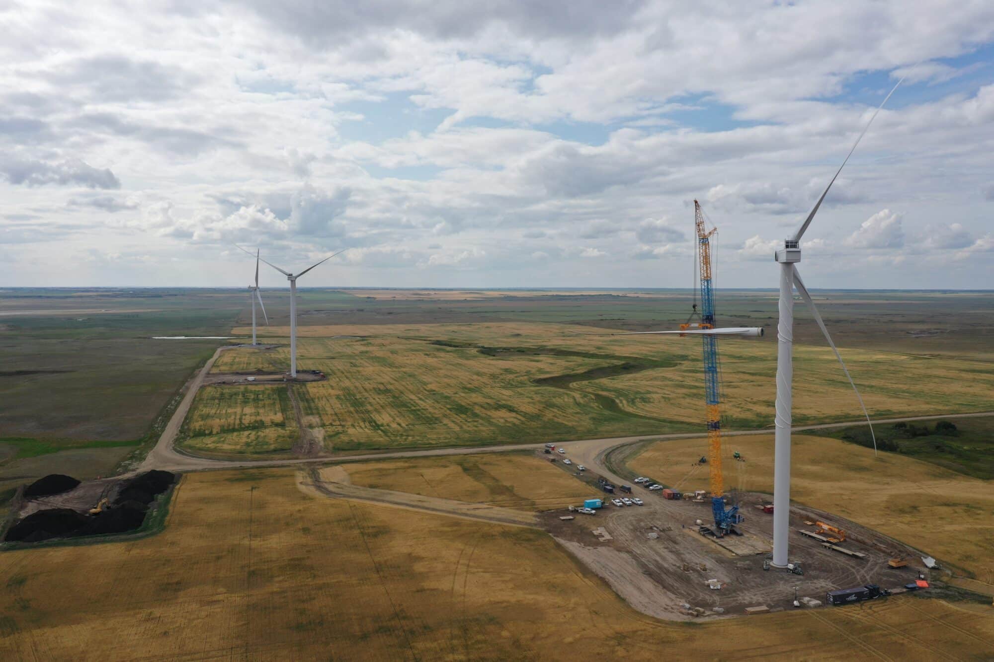 Landscape photo of three wind turbine in a green field, a crane stands next to one turbine under construction.