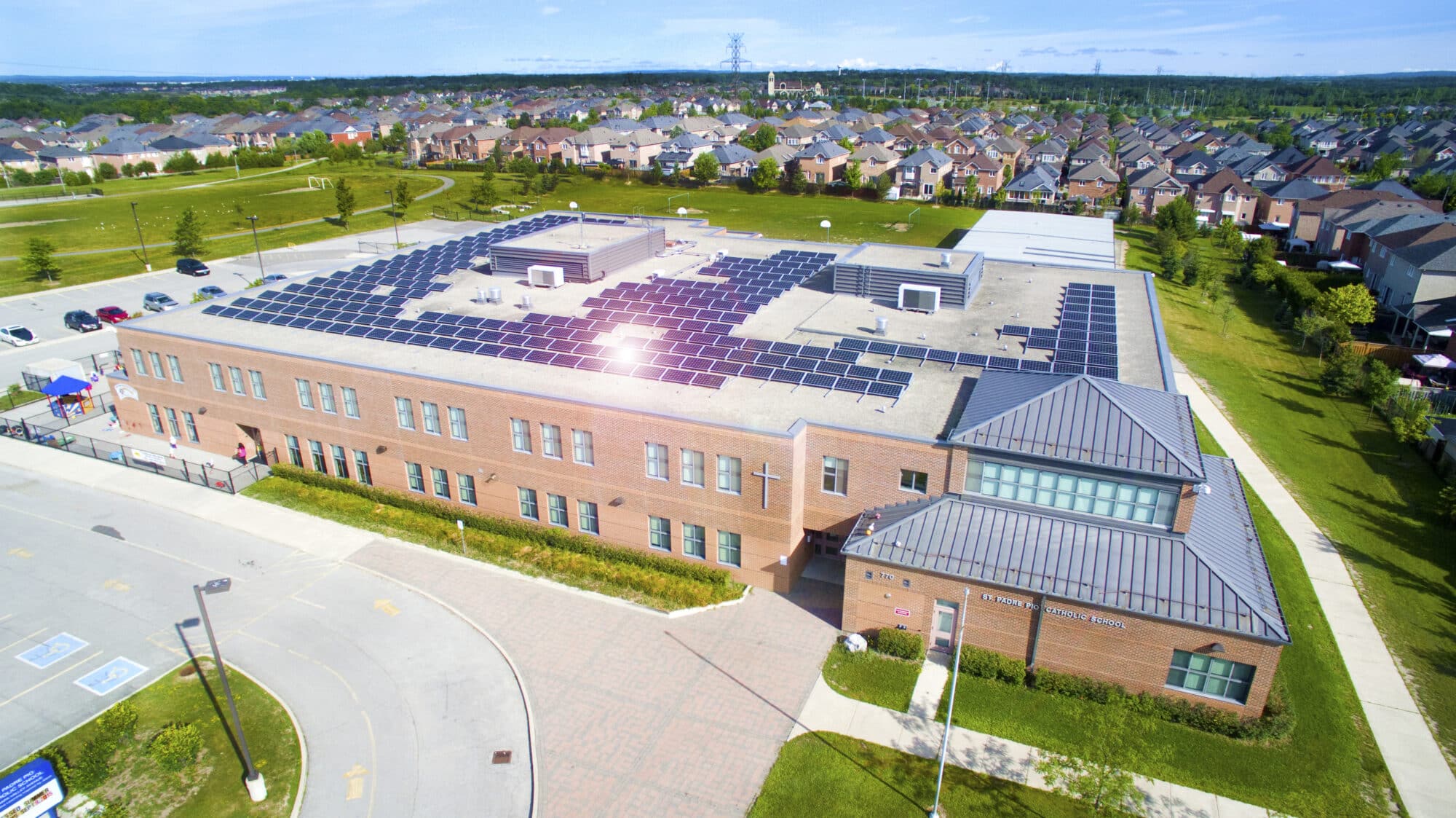 School in the suburbs that has rooftop solar panels spread across the roof. The sun is reflecting off the panels.
